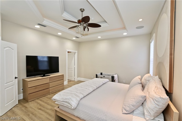 bedroom with ceiling fan, a tray ceiling, and light wood-type flooring