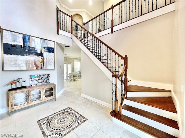 staircase featuring a towering ceiling, ornamental molding, and light tile flooring