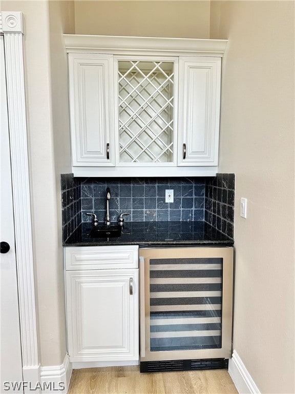 bar with beverage cooler, light hardwood / wood-style floors, tasteful backsplash, and white cabinetry