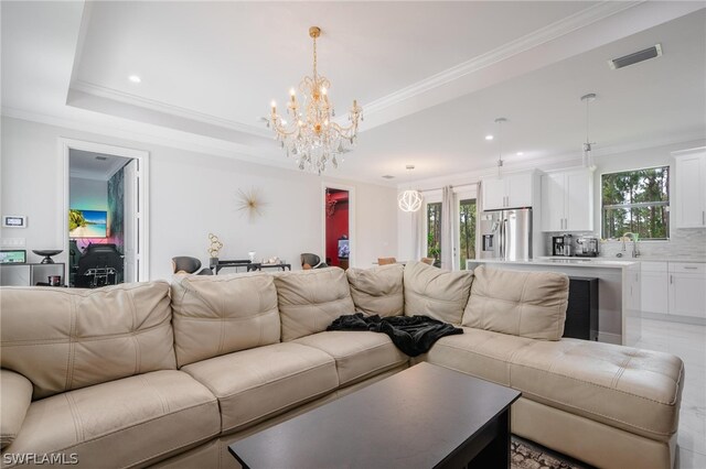 living room with ornamental molding, a tray ceiling, and an inviting chandelier