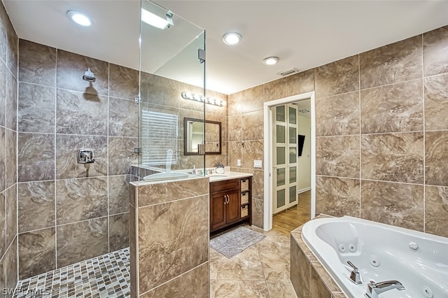 bathroom with shower with separate bathtub, vanity, and tile walls