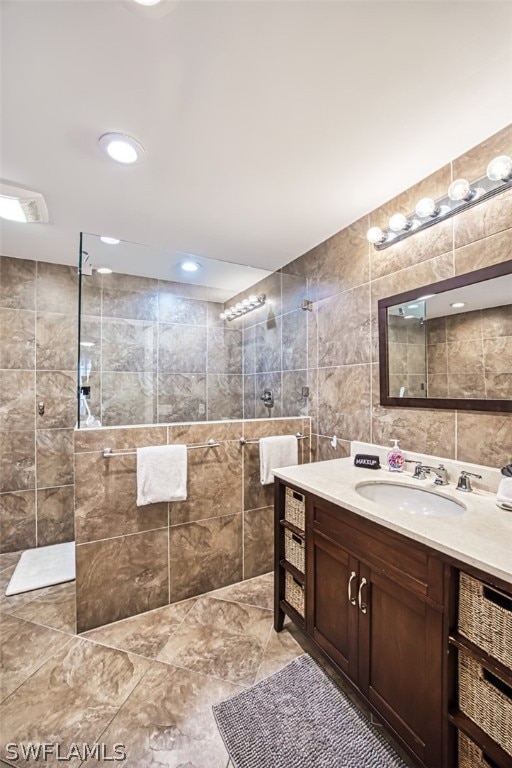 bathroom with a tile shower, vanity, and tile walls