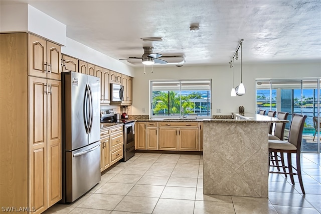 kitchen with stainless steel appliances, ceiling fan, pendant lighting, a breakfast bar area, and light tile patterned flooring