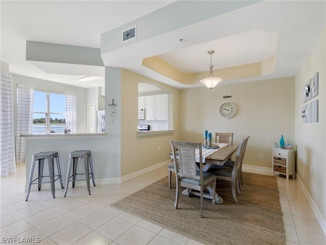 dining area featuring a tray ceiling and light tile patterned flooring