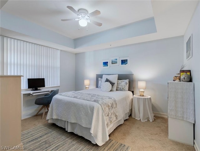 bedroom featuring ceiling fan, light carpet, and a tray ceiling