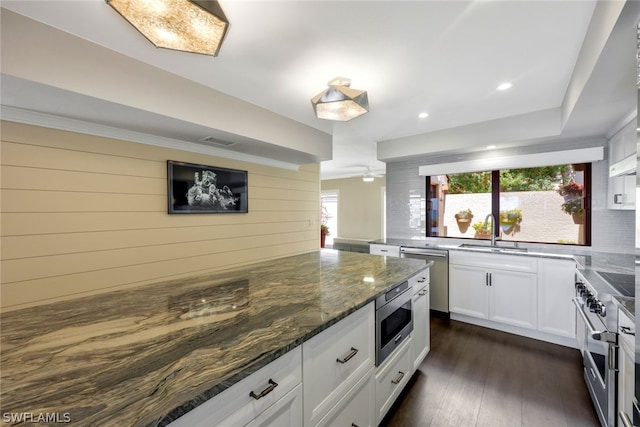 kitchen featuring appliances with stainless steel finishes, dark stone counters, sink, dark hardwood / wood-style floors, and white cabinetry