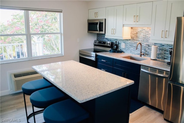 kitchen with an AC wall unit, white cabinetry, sink, stainless steel appliances, and light stone countertops