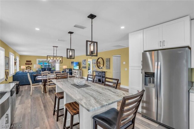 kitchen featuring stainless steel refrigerator with ice dispenser, a kitchen bar, white cabinetry, decorative light fixtures, and light stone countertops