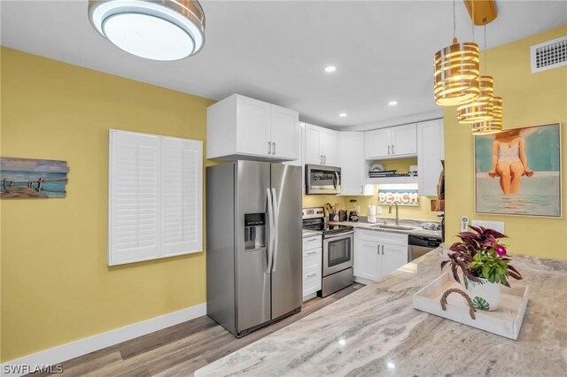 kitchen with appliances with stainless steel finishes, white cabinetry, sink, hanging light fixtures, and light hardwood / wood-style flooring