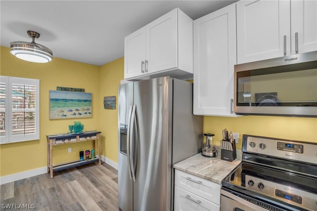 kitchen featuring white cabinetry, light stone countertops, stainless steel appliances, and light hardwood / wood-style floors