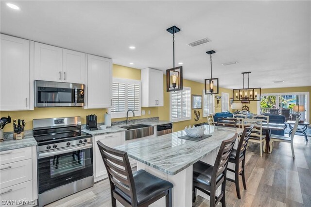 kitchen featuring sink, a breakfast bar area, stainless steel appliances, white cabinets, and a kitchen island