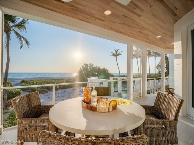 sunroom / solarium with plenty of natural light, a water view, wooden ceiling, and a view of the beach