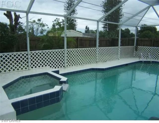 view of swimming pool featuring glass enclosure and an in ground hot tub