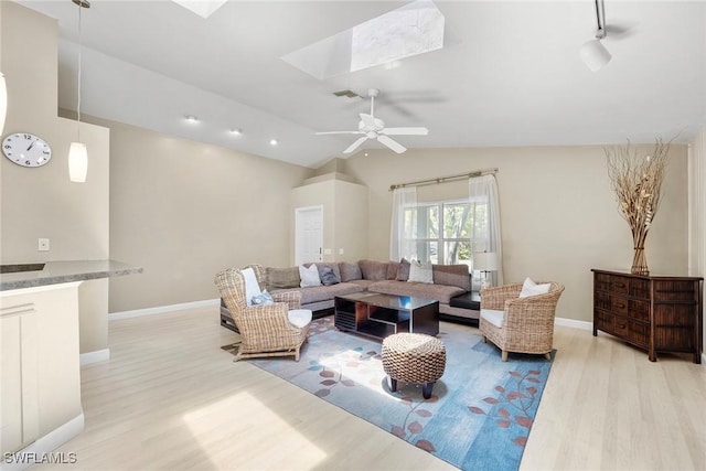 living room with vaulted ceiling with skylight, ceiling fan, and light hardwood / wood-style flooring