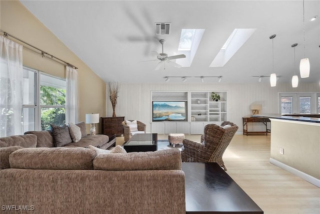 living room with light hardwood / wood-style flooring, built in features, ceiling fan, vaulted ceiling with skylight, and track lighting