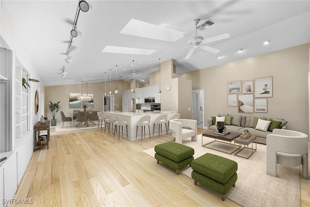 living room featuring a skylight, rail lighting, sink, ceiling fan, and light hardwood / wood-style floors