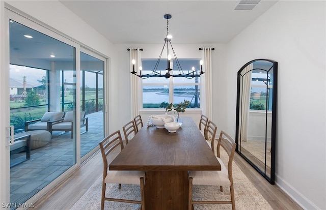 dining area with an inviting chandelier, light wood-type flooring, and a water view