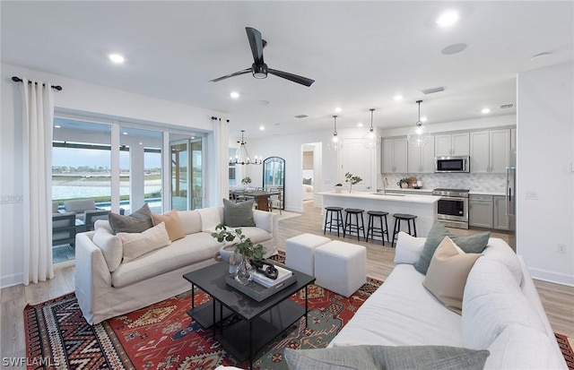 living room featuring ceiling fan with notable chandelier, light hardwood / wood-style floors, and sink