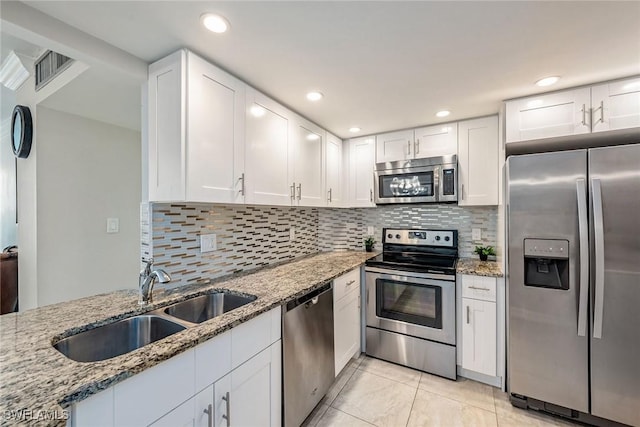 kitchen with a sink, white cabinets, light stone counters, and stainless steel appliances