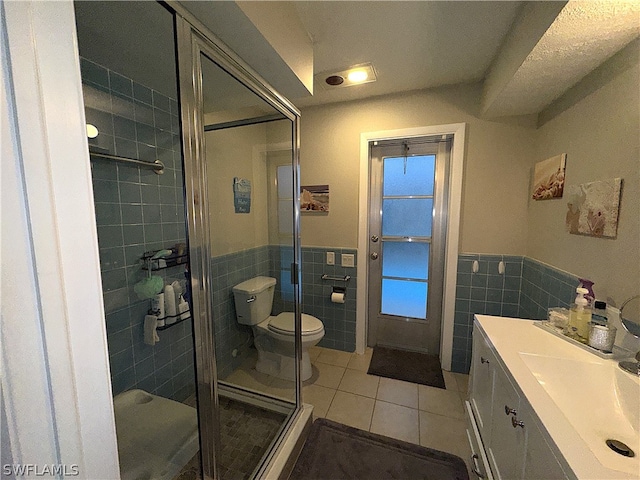 bathroom featuring toilet, tile patterned floors, tile walls, a shower with door, and vanity