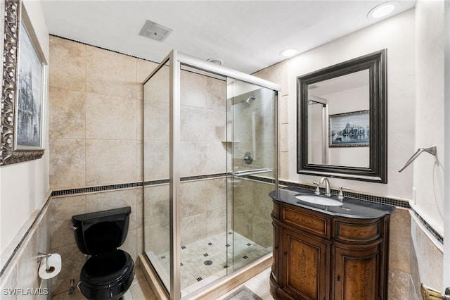 bathroom featuring vanity, a shower with shower door, toilet, and tile walls