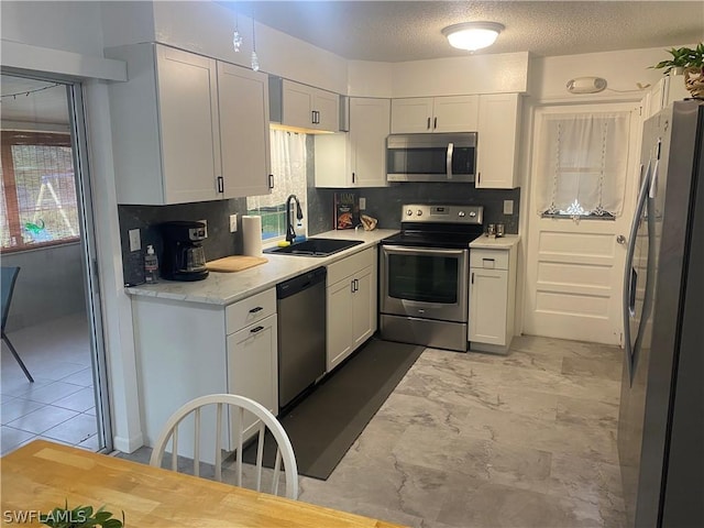 kitchen featuring a textured ceiling, a sink, white cabinetry, appliances with stainless steel finishes, and decorative backsplash