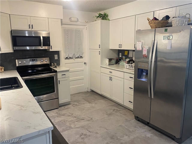 kitchen with white cabinets, stainless steel appliances, light stone counters, and backsplash