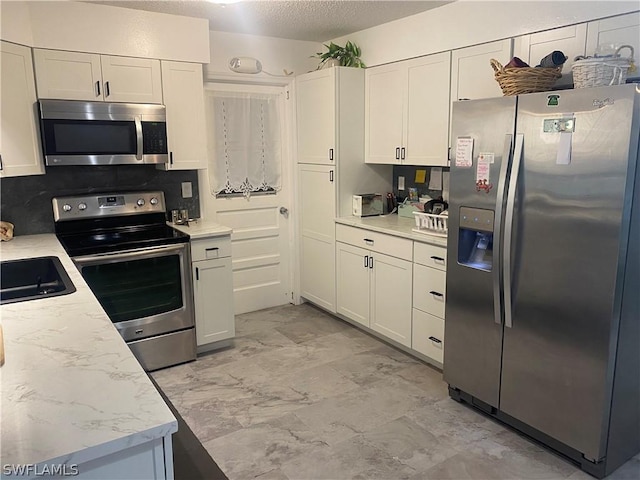 kitchen featuring marble finish floor, appliances with stainless steel finishes, white cabinetry, a sink, and a textured ceiling