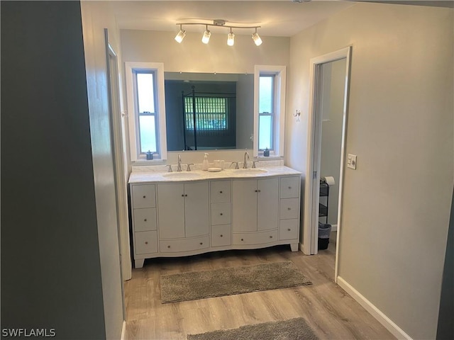 full bathroom featuring double vanity, a sink, baseboards, and wood finished floors