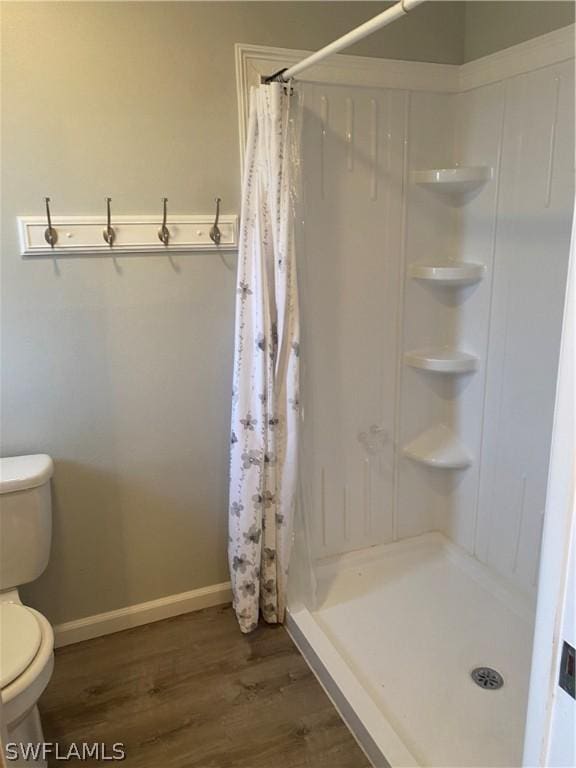 bathroom featuring toilet, a stall shower, baseboards, and wood finished floors