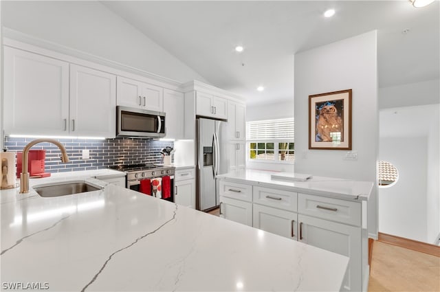 kitchen featuring light stone countertops, stainless steel appliances, sink, white cabinetry, and lofted ceiling