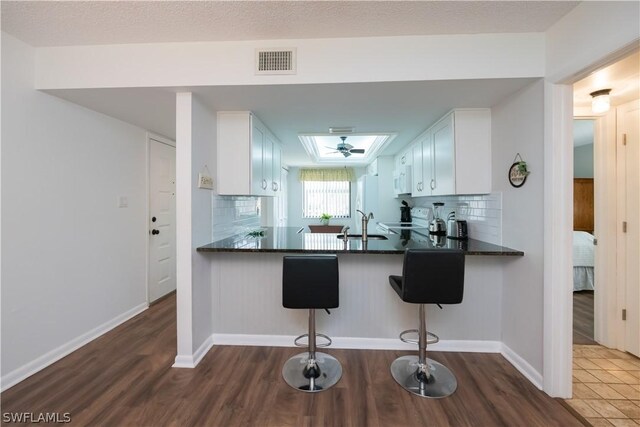 kitchen featuring dark wood-type flooring, a kitchen breakfast bar, decorative backsplash, white cabinetry, and kitchen peninsula