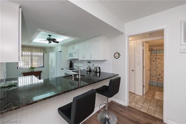 kitchen featuring white appliances, dark stone counters, kitchen peninsula, dark hardwood / wood-style flooring, and white cabinetry