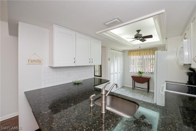 kitchen with a tray ceiling, dark stone countertops, sink, and white cabinets