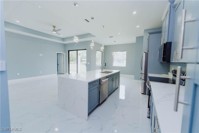 kitchen featuring a kitchen island with sink, sink, hanging light fixtures, light stone counters, and stainless steel appliances