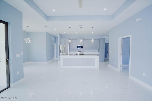 kitchen with a tray ceiling, sink, a center island with sink, and appliances with stainless steel finishes