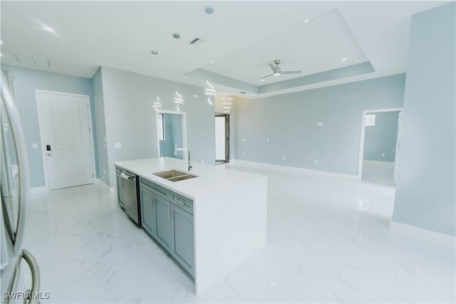 kitchen featuring ceiling fan, dishwasher, sink, a tray ceiling, and a center island with sink