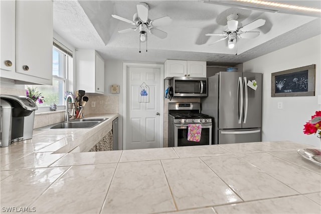 kitchen with stainless steel appliances, white cabinets, sink, and ceiling fan