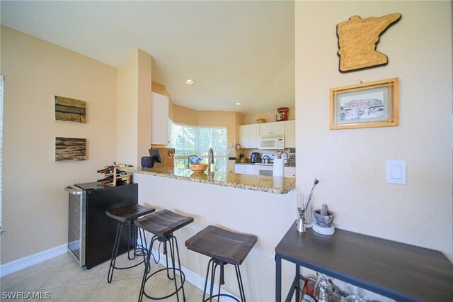 kitchen with kitchen peninsula, light stone counters, light tile patterned floors, white cabinets, and a breakfast bar area