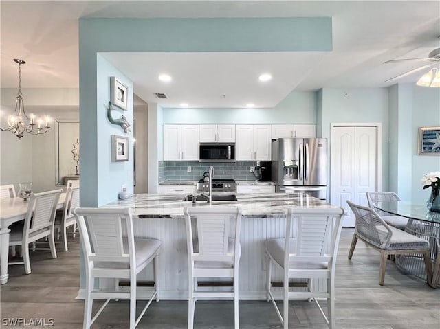 kitchen with tasteful backsplash, light stone counters, stainless steel appliances, white cabinets, and hanging light fixtures