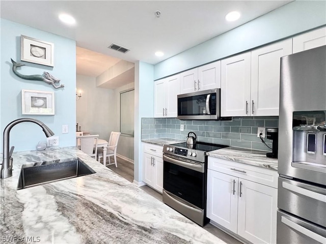 kitchen with decorative backsplash, appliances with stainless steel finishes, light stone counters, sink, and white cabinetry