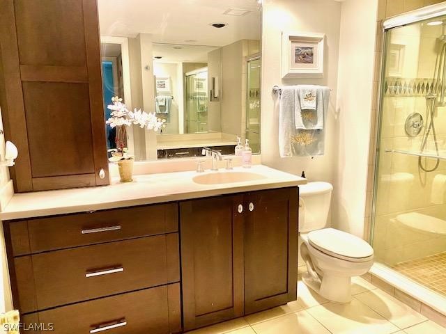 bathroom featuring tile patterned flooring, vanity, toilet, and a shower with door