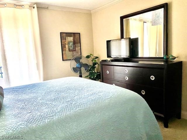 bedroom with ornamental molding and light colored carpet