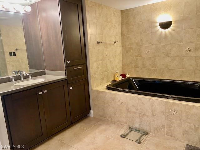 bathroom featuring vanity, a relaxing tiled tub, tile patterned floors, and tile walls