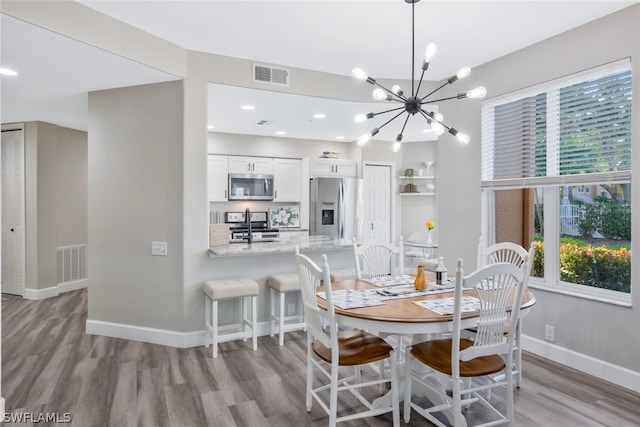 dining area with sink, light hardwood / wood-style flooring, and a notable chandelier