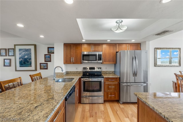 kitchen with light wood-type flooring, stainless steel appliances, a tray ceiling, and sink