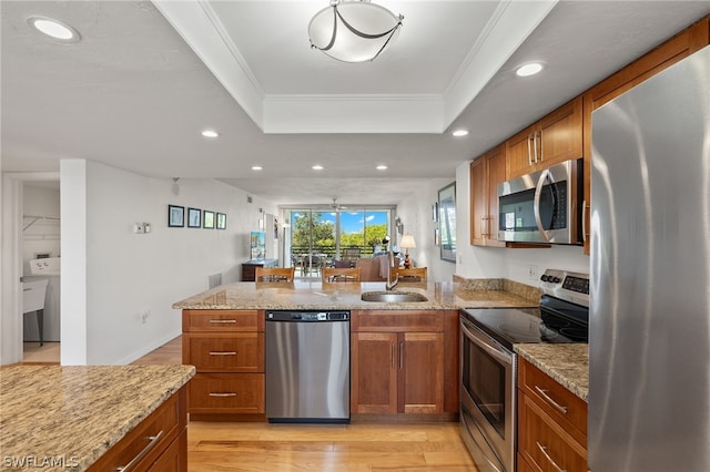 kitchen with sink, stainless steel appliances, a raised ceiling, light hardwood / wood-style flooring, and ornamental molding