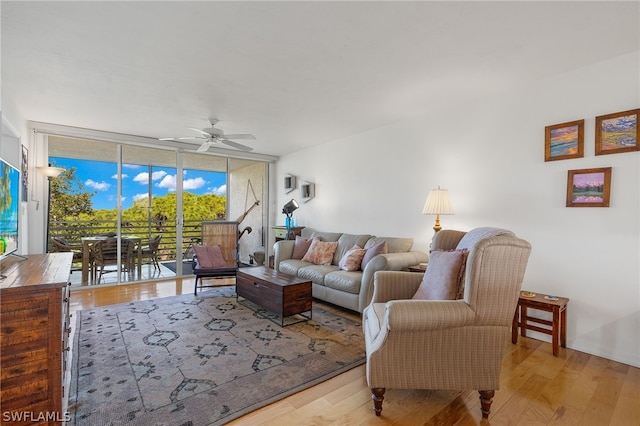 living room featuring ceiling fan, light wood-type flooring, and a wall of windows