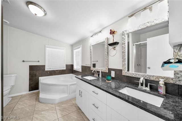 bathroom with tile patterned floors, dual vanity, a tub to relax in, vaulted ceiling, and toilet