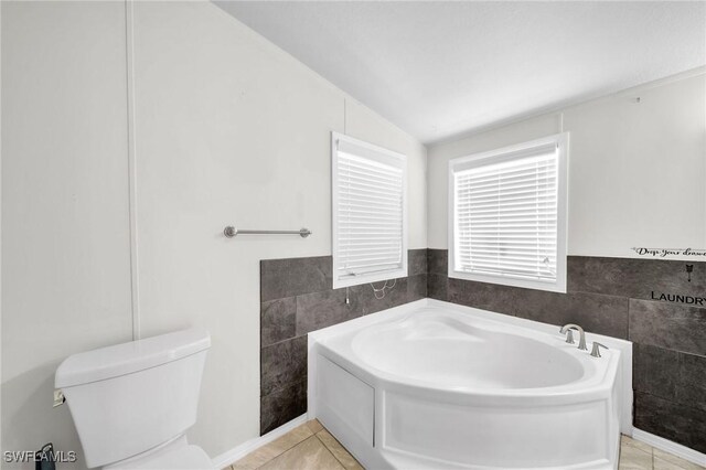 bathroom with a washtub, lofted ceiling, toilet, and tile walls